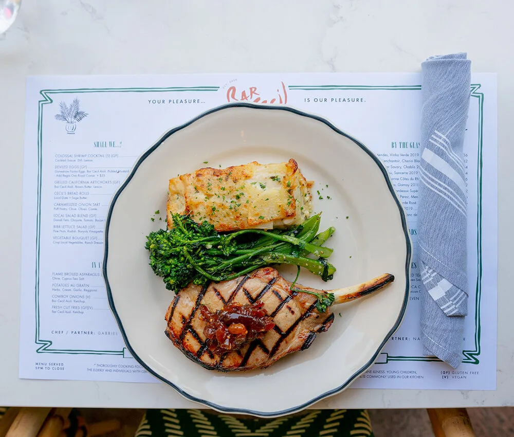 A grilled pork chop, potatoes au gratin, and broccolini served over a Bar Cecil menu.