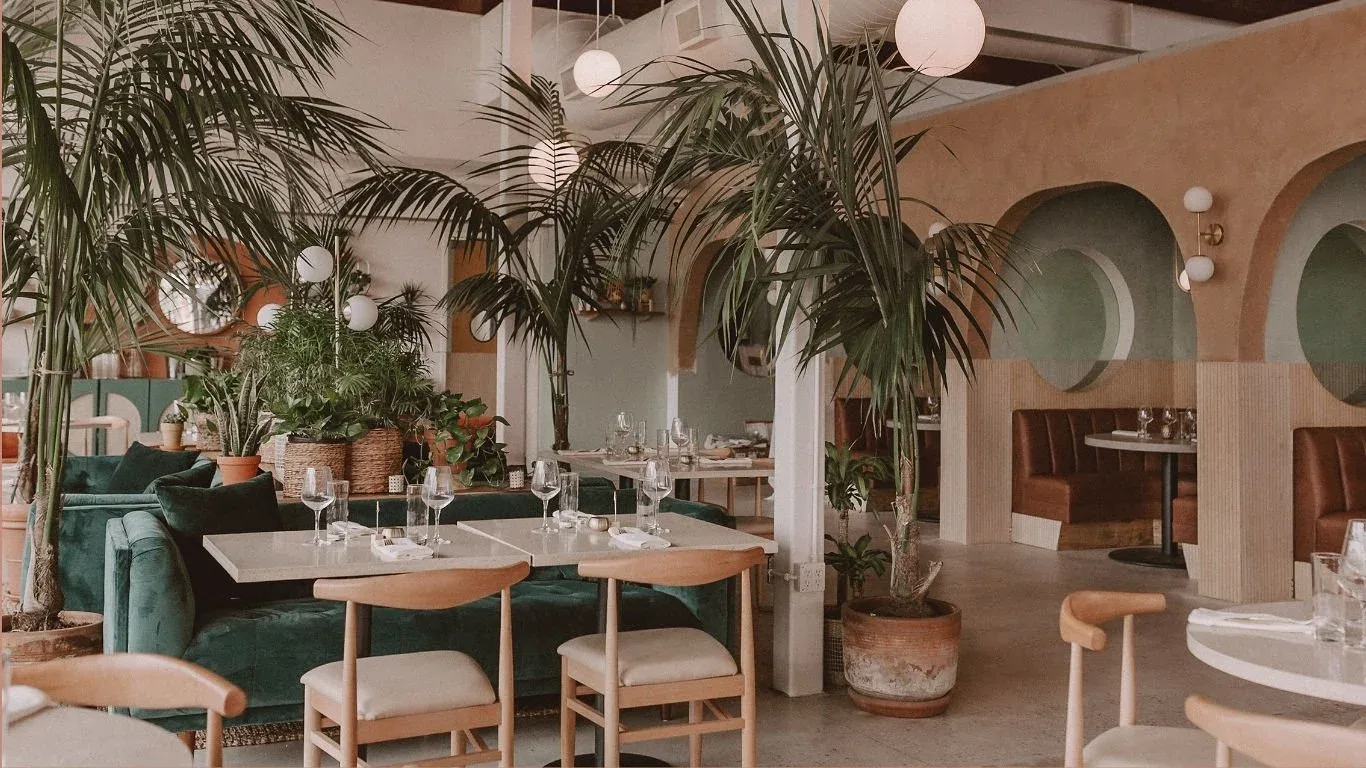 Boozehounds’ plant-filled dining room with green banquettes and arched booths.