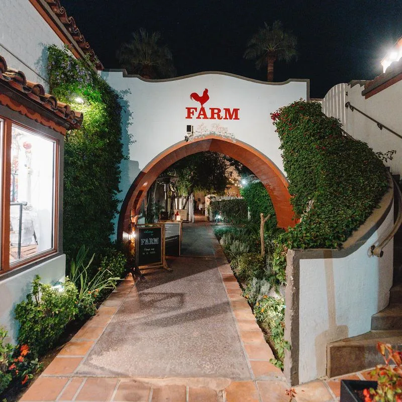 FARM’s red-lettered entrance rises above an arched walkway framed by greenery at night.