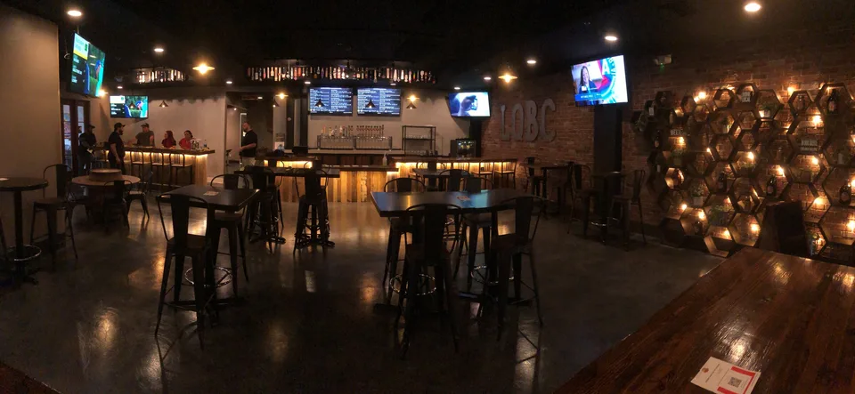 A warmly lit La Quinta Brewing taproom has a long bar, rows of tap handles, and tables arranged across the room.