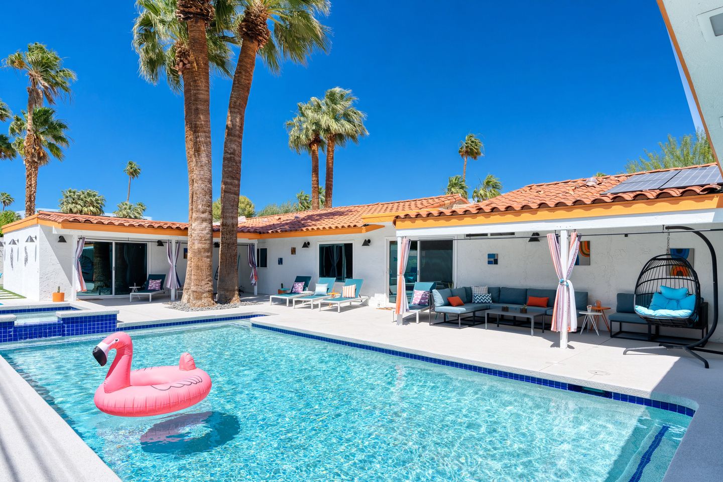 Turquoise pool with a pink flamingo float beneath tall Palm Springs palms