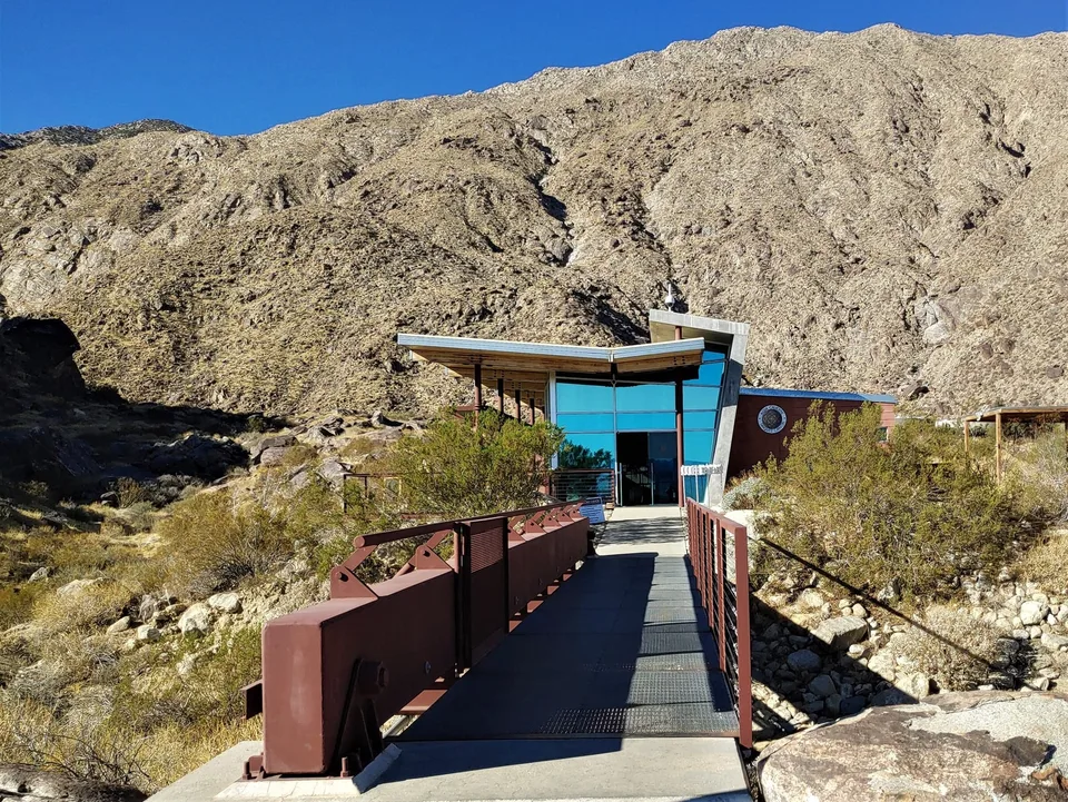 A footbridge leads to the Tahquitz Canyon Visitor Center beneath bare desert mountains.