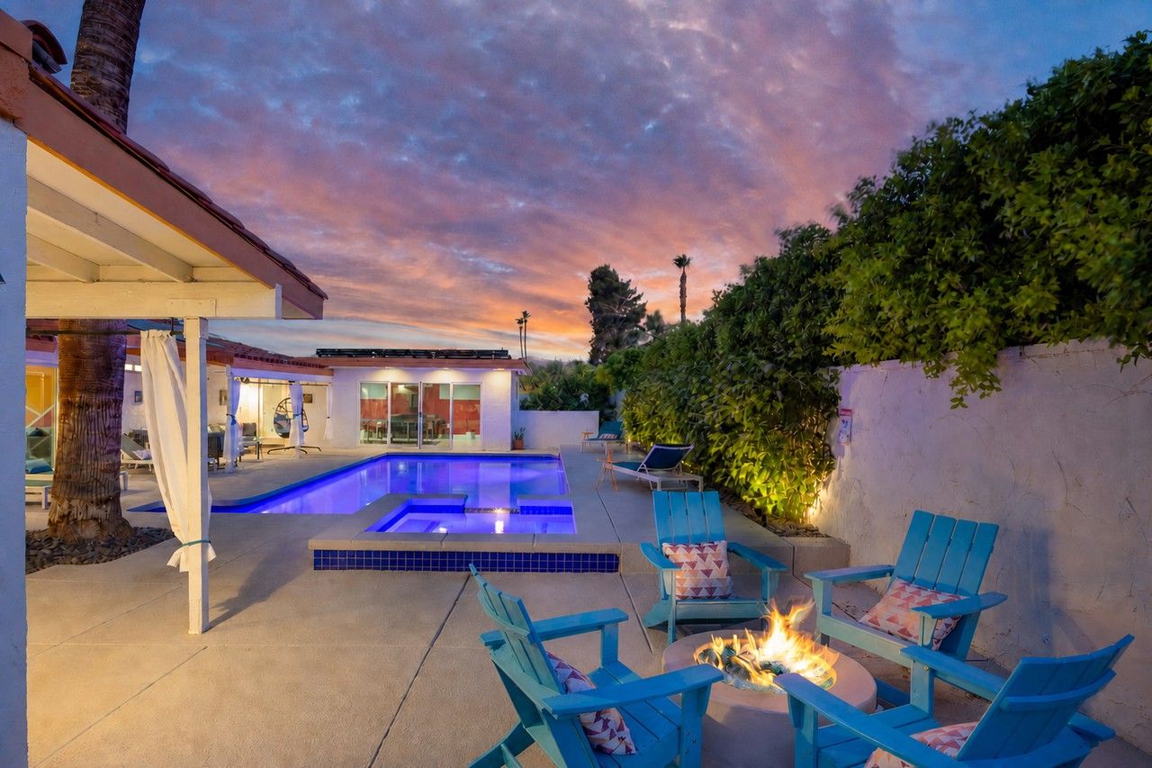 Twilight pool courtyard with turquoise chairs around a lit fire pit beneath a pink desert sky